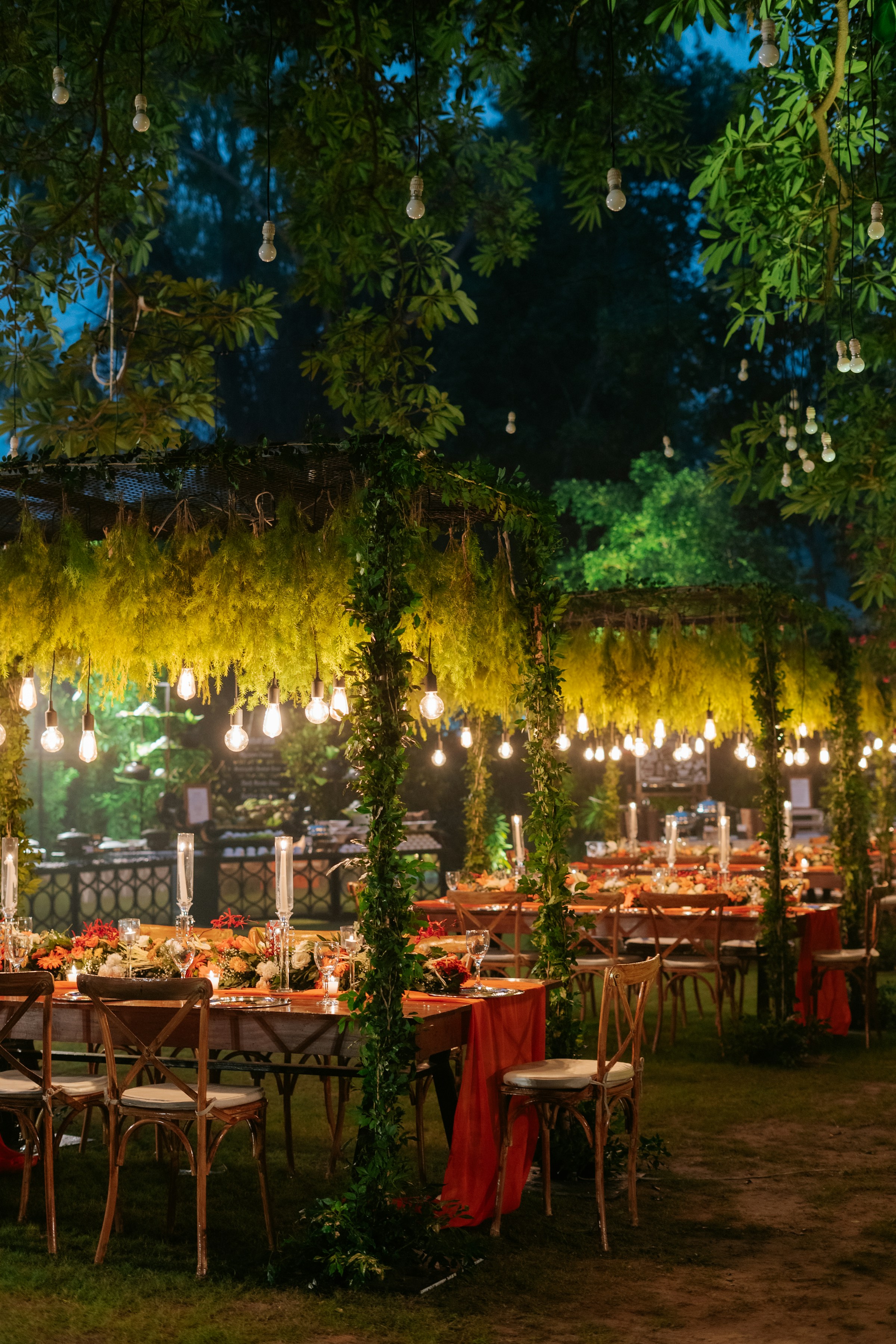 A long outdoor dinner table beneath trees and warm hanging lights