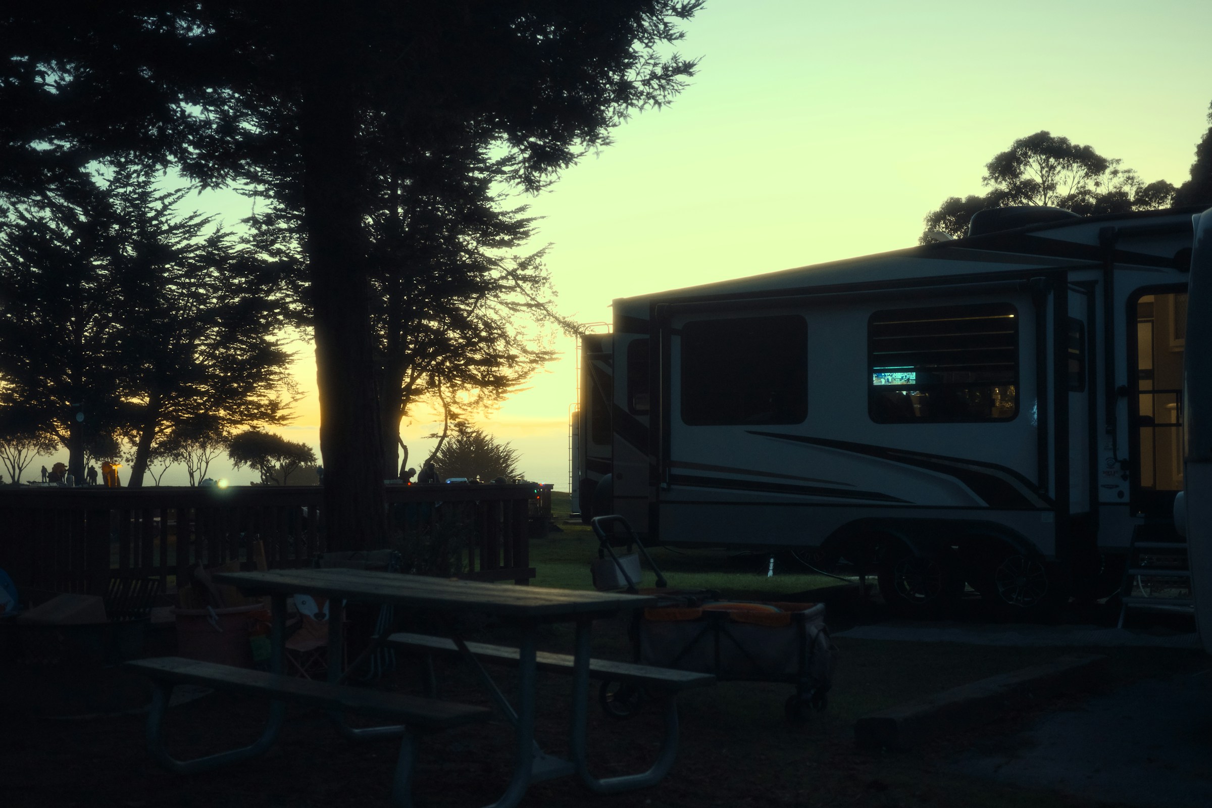 An RV beside picnic tables and trees at sunset